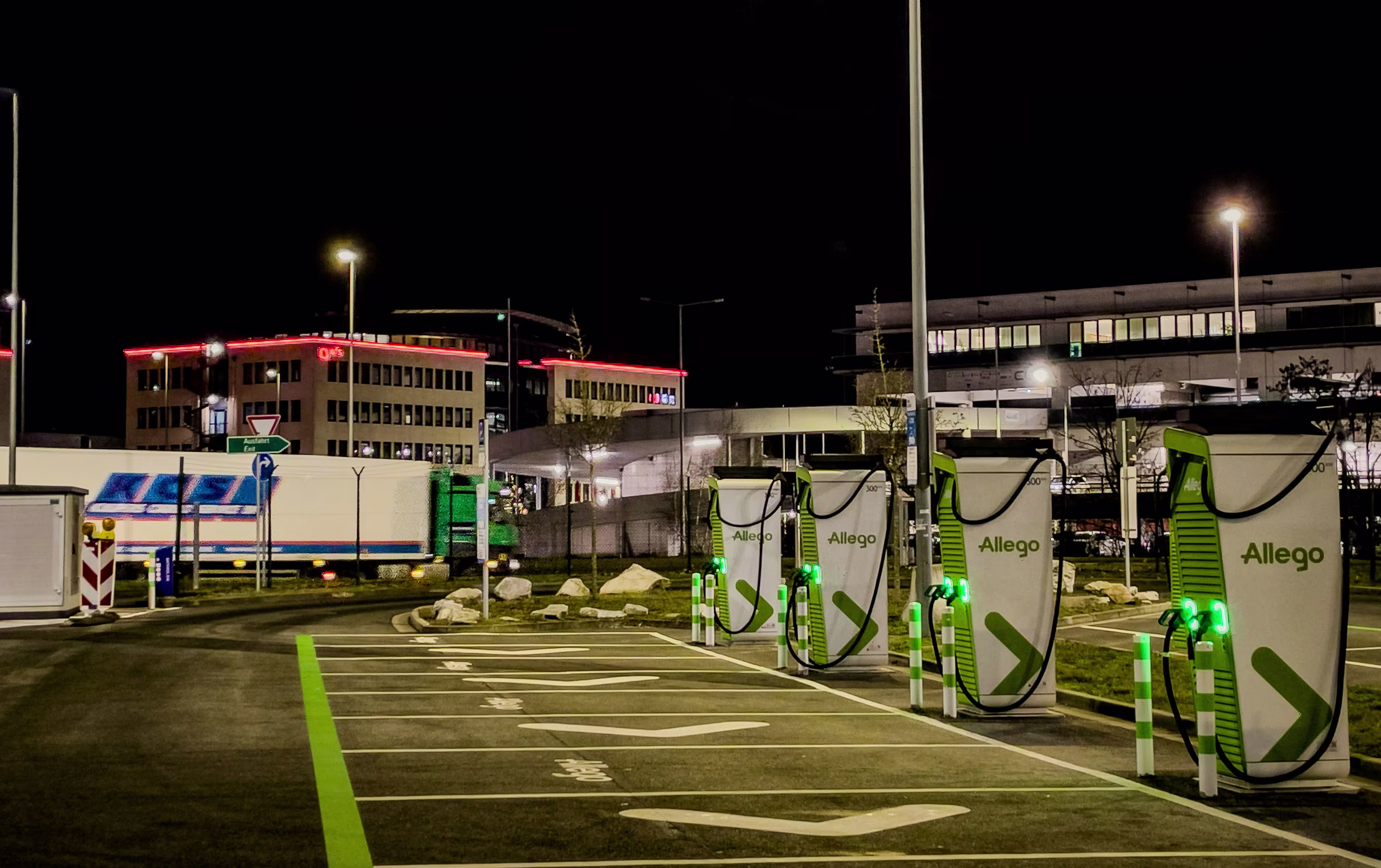 A row of Allego electric vehicle fast-charging stations in an empty parking lot lit up at night